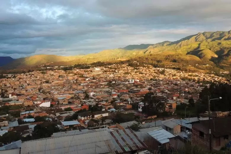 Panorámica del pueblo de Huancas, montado sobre mesetas andinas y rodeado de vegetación, con la iglesia colonial visible en el centro.