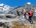Senderistas caminando en la Cordillera Blanca con laguna y nevados de fondo.