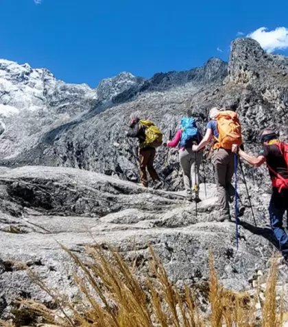 Senderistas caminando en la Cordillera Blanca con laguna y nevados de fondo.