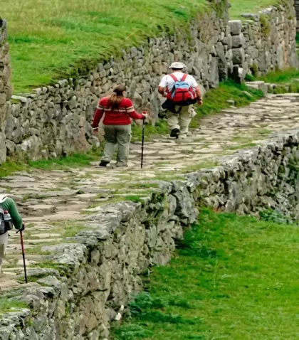 Turistas caminan por un sendero de piedra rodeado de muros incas y paisajes verdes, una experiencia cl�sica del turismo de aventura en Cusco.